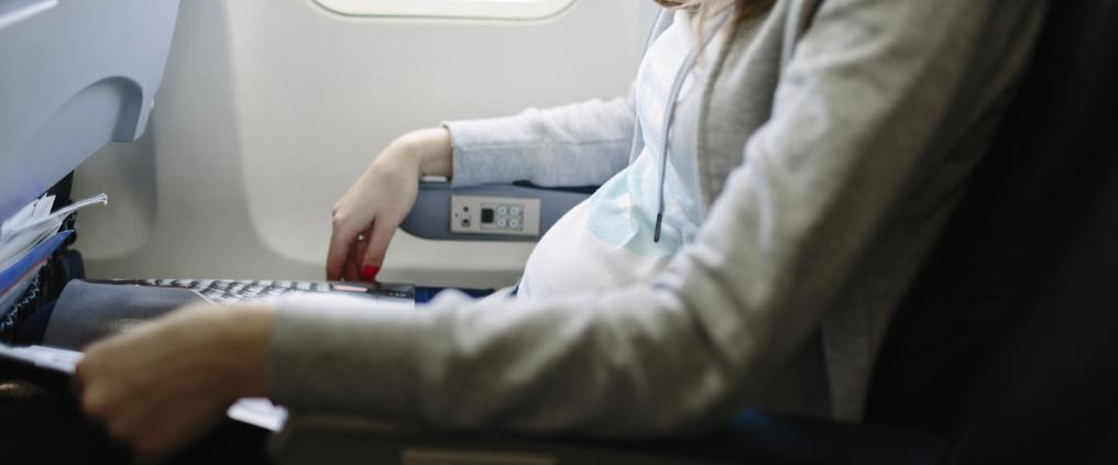 Close up of pregnant passengers belly while she sits in airplane cabin.