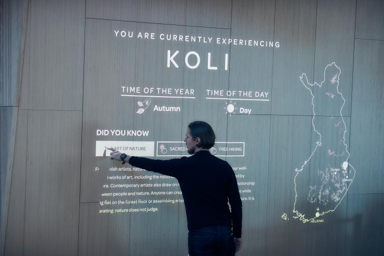 Mies käyttää seinälle heijastettua interaktiivista valoheijastusta informaation näyttämiseen Helsinki-Vantaa lentokentän Aukiolla.