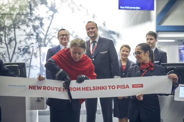 Norwegianin henkilökunnan jäsen leikkaamassa seremonianauhaa portilla, reittiavajaisissa.