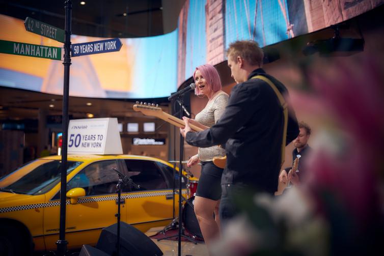 Nainen laulaa ja mies soittaa kitaraa New York teemaisessa tapahtumassa.