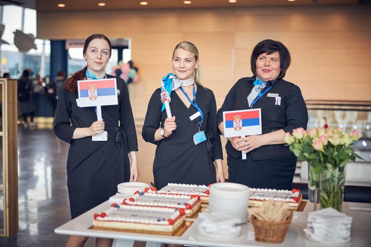 Three Air Serbia staff holding flag of Serbia at route opening event.