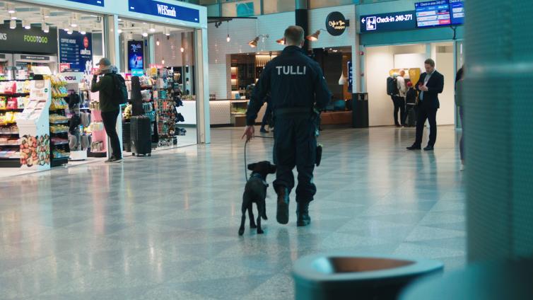 Customs sniffer dog and customs officer walking in Helsinki Airport's departure hall.
