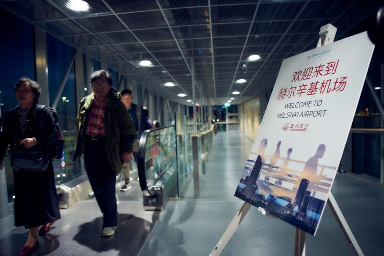 Sichuan Airlinesin matkustajia saapumassa Helsinki-Vantaalle reitinavauksesta kertovan kyltin ohi. 