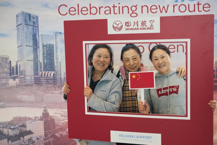 Kolme naista pitelee Sichuan Airlinesin ja Helsinki-Vantaan punaista kehystä ympärillään kuvausseinän luona. 