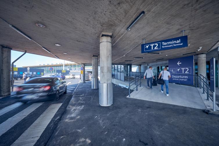 Car passing by and passenger walking towards entry at Helsinki Airport.