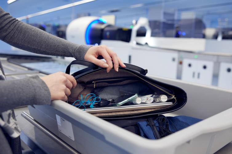 A passenger sets their hand luggage on a tray for security check