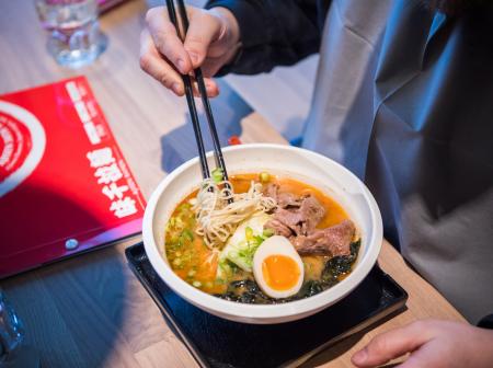 Puikkoja pitelevä käsi ja Ajisen Ramenin nuudelikulho.