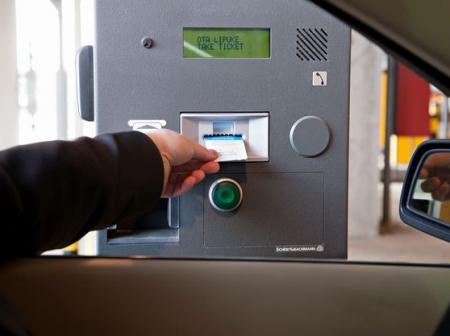 Käsi kurottautuu autosta ottamaan lipukkeen pysäköintiautomaatilta.