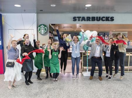 Starbucks staff celebrating ribbon cutting at coffee shop's grand opening.