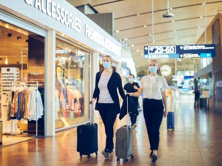 Matkustajia pukeutuneena maskiin Helsinki-Vantaalla