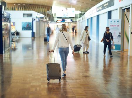 Nainen kävelee lentoasemalla vetäen laukkua. 