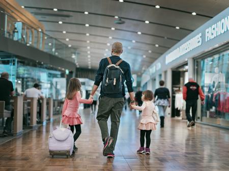 Isä kävelee yhdessä tyttöjen kanssa lentoasemalla.