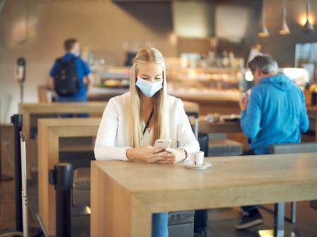 Tyttö selaa kännykkää kahvilassa.