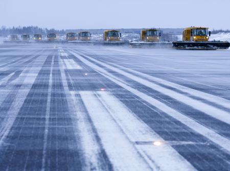 Talvikunnossapitokalusto puhdistaa kiitotietä pitkänä letkana.