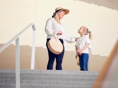 Nainen ja lapsi seisovat lentoaseman lähtöaulassa, portaiden yläpäässä ja katsovat toisiinsa.
