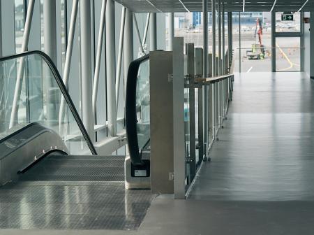 Liukuportaat ja ulko-ovi lasiseinäisellä käytävällä.