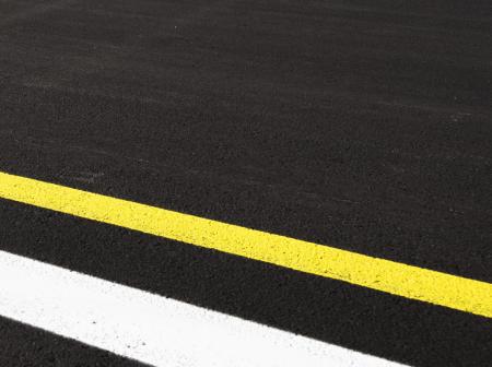 Lähikuva mustasta kiitotieasfaltista, jossa on keltainen ja valkoinen viiva.