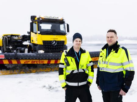 Kaksi keltaliivistä työntekijää seisoo ison, keltaisen kunnossapitoauton edessä.