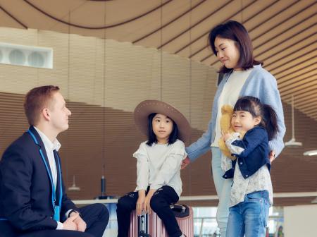 Perhe jossa äiti ja kaksi lasta Helsinki-Vantaan lentokentällä asiakaspalvelijan kanssa