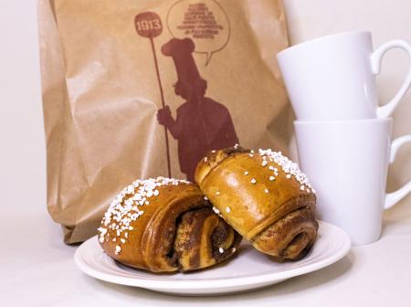 Kuvassa kahvimukeja, pullaa ja paperipussi.