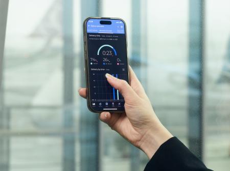 Käsi pitelee puhelinta, jonka näytöllä on AOS-järjestelmän mittareita.