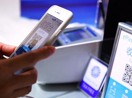 Passenger scanning Alipay QR-code with a smartphone at cash register.