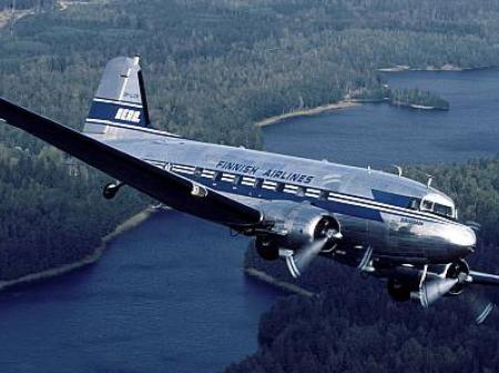 Vanha lentokone lentää metsän ja järven ylitse.