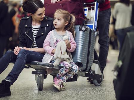 A woman and a child sitting on a suicase cart.