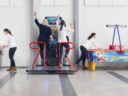 Two people trying different arcade games at Helsinki airport.