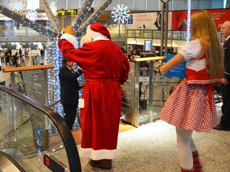 Santa Claus waves at passengers as choir sings next to him.