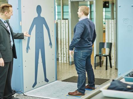 A man standing at a body scanner at airport security.