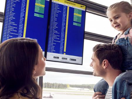 Family of three looking for their flight from flight departure timetable display. 