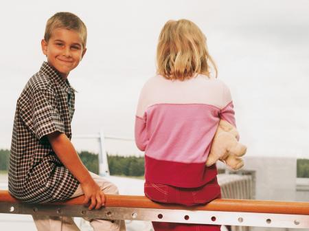 Two children sitting on a railing to look at airplanes through a window. Boy is turned around smiling.