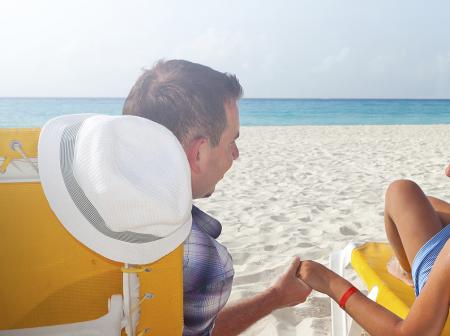 Couple lounging on sunlounges on a beach holding hands