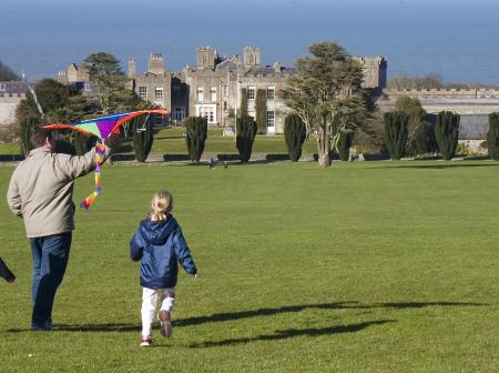 Father and two children are about to fly a kite in grasslands with a castle in the background.