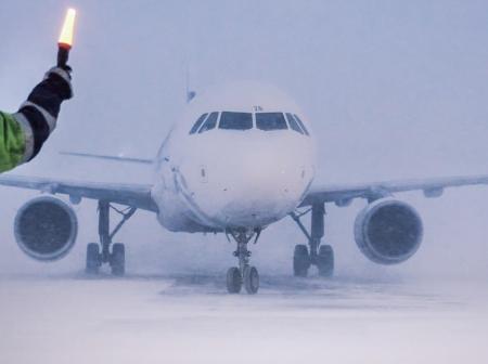 A man guiding airplane with light in a snowstorm.