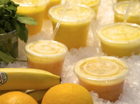 Fruits and berries next to freshly made juices in takeaway plastic cups.