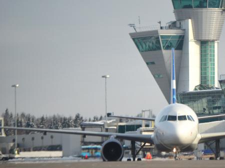 Airplane from front with air traffic control tower behind it.