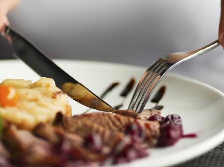 Closeup of hands holding knife and fork cutting steak to eat.