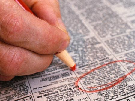 Käsi ympyröi kynällä työpaikkailmoituksen sanomalehdestä.