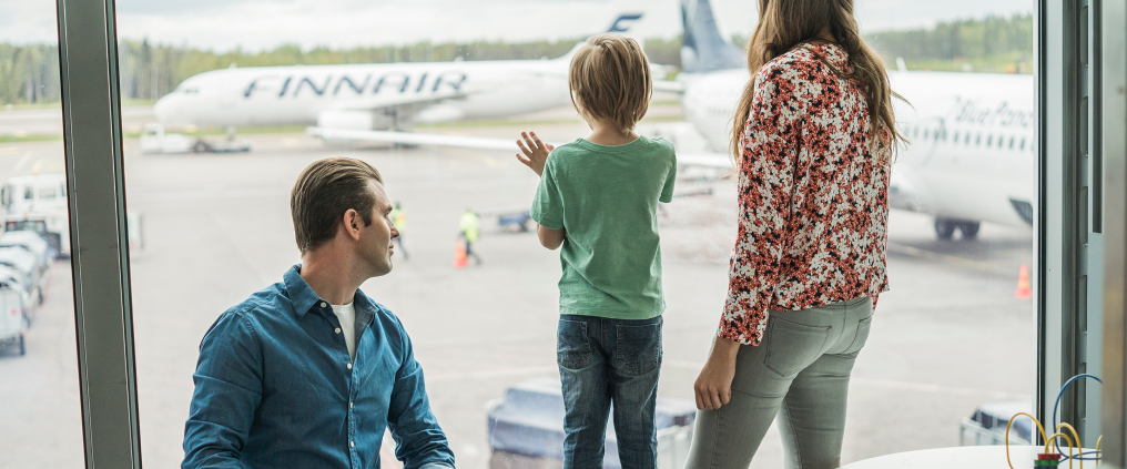 Perhe katselemassa lentokoneita terminaalin ikkunasta.
