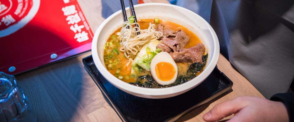 Closeup of Ajisen Ramen tonkatsu ramen bowl with a hand holding chopsticks.