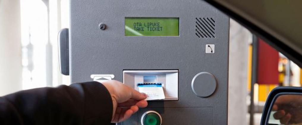 Käsi kurottautuu autosta ottamaan lipukkeen pysäköintiautomaatilta.