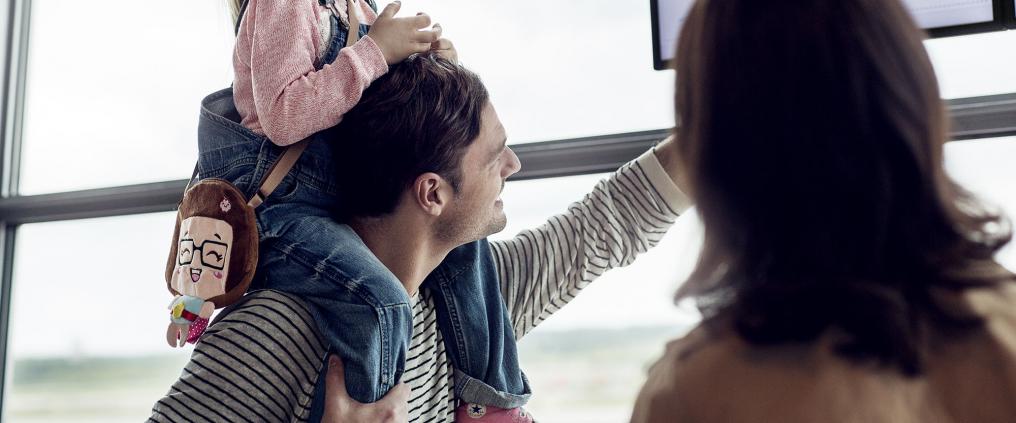Family of three looking for their flight from flight departure timetable display. 