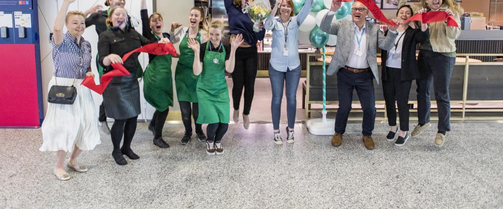 Starbucks staff celebrating ribbon cutting at coffee shop's grand opening.
