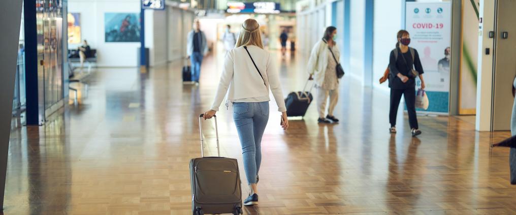 Nainen kävelee lentoasemalla vetäen laukkua. 