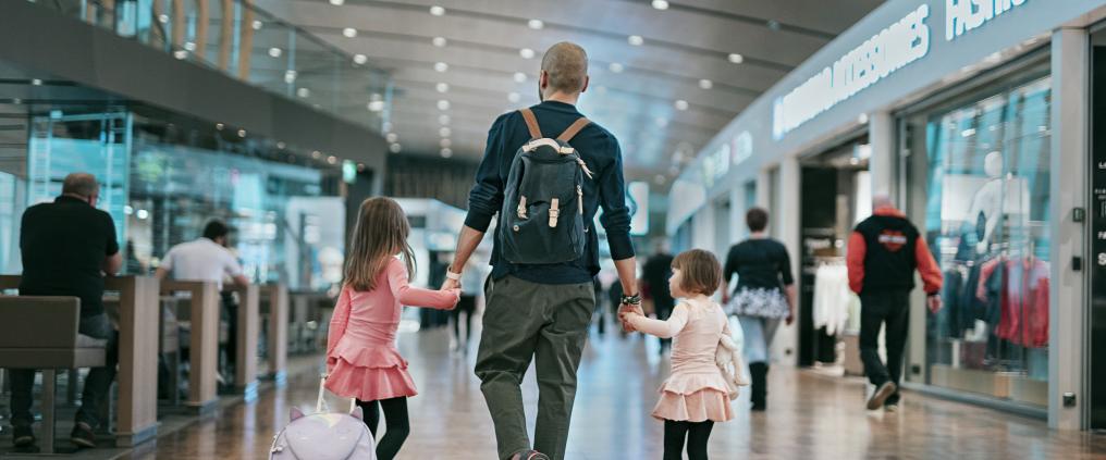 Isä kävelee yhdessä tyttöjen kanssa lentoasemalla.