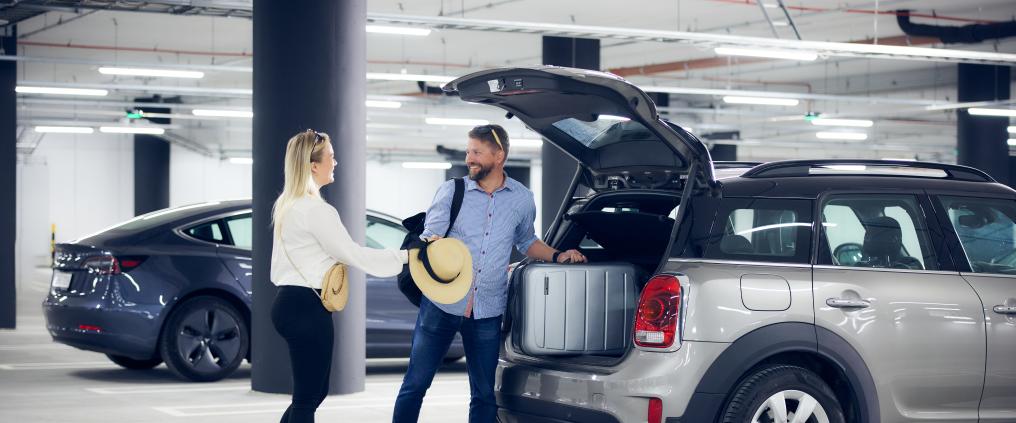 Pariskunta nostaa matkalaukkunsa autostaan pysäköintihallissa