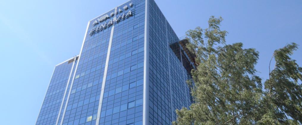 Korkea, sinisävyinen, lasiseinäinen toimistorakennus, jonka vieressä koivu ja takana sininen taivas.