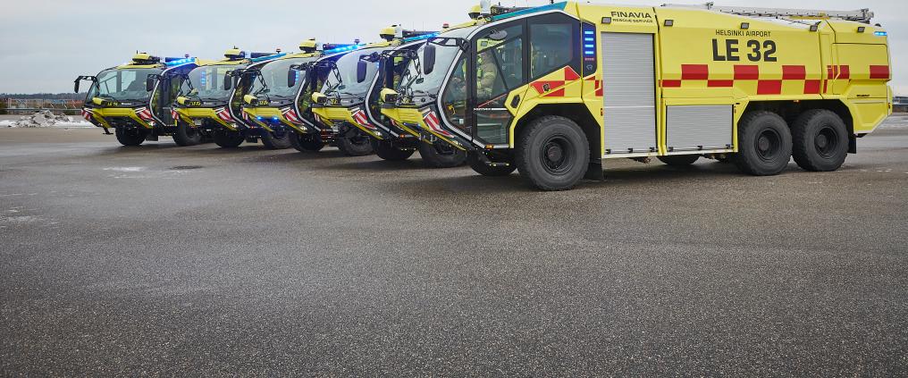 Rivi isoja, keltaisia sammutusautoja lentoasemalla.